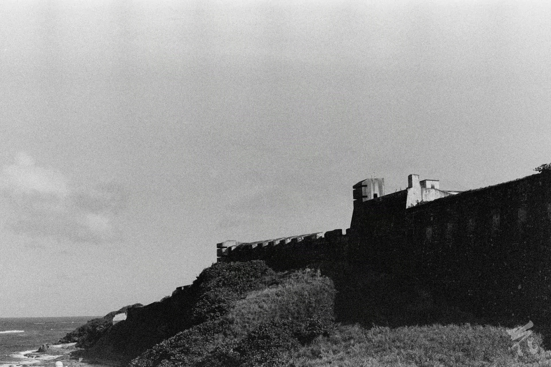 A black-and-white analog photograph of a fortress next to the sea.