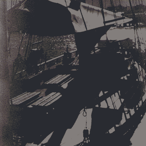 A black and white analog photograph. Stark contrast shows shadows cast by the sun reflecting off the deck of a boat opposite to where the picture was taken. Many sails, wooden pallets and barrels line the deck. In the foreground, ropes go up to the mast.